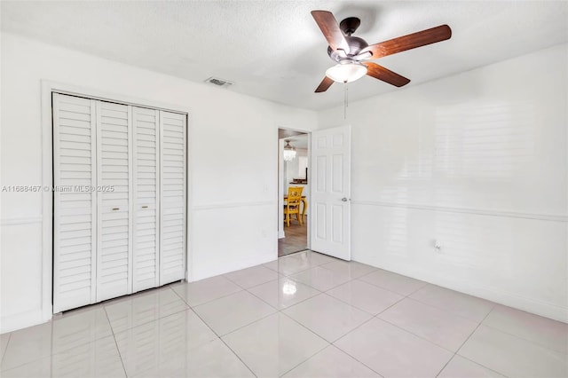 unfurnished bedroom featuring ceiling fan, a closet, light tile patterned flooring, and a textured ceiling