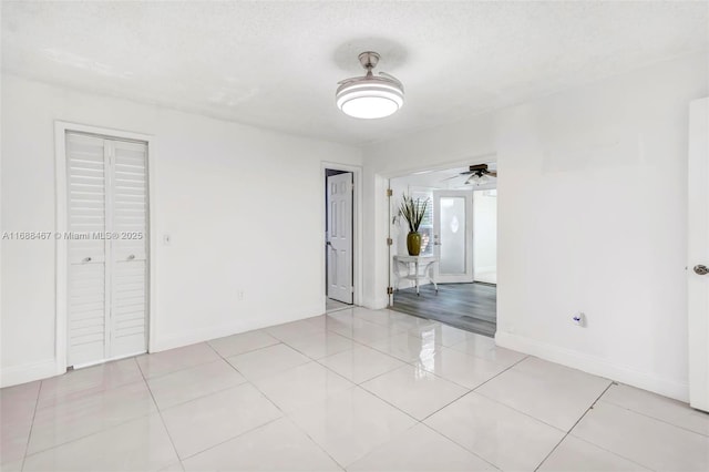 spare room featuring ceiling fan, light tile patterned flooring, and a textured ceiling