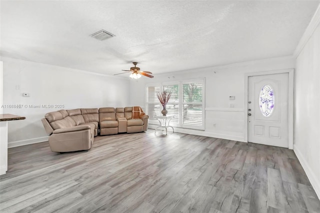 unfurnished living room featuring ceiling fan, ornamental molding, a textured ceiling, and light hardwood / wood-style flooring