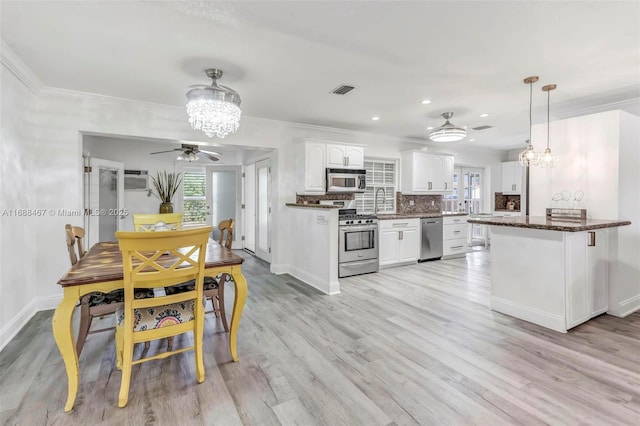 kitchen featuring stainless steel appliances, tasteful backsplash, decorative light fixtures, white cabinets, and ceiling fan with notable chandelier