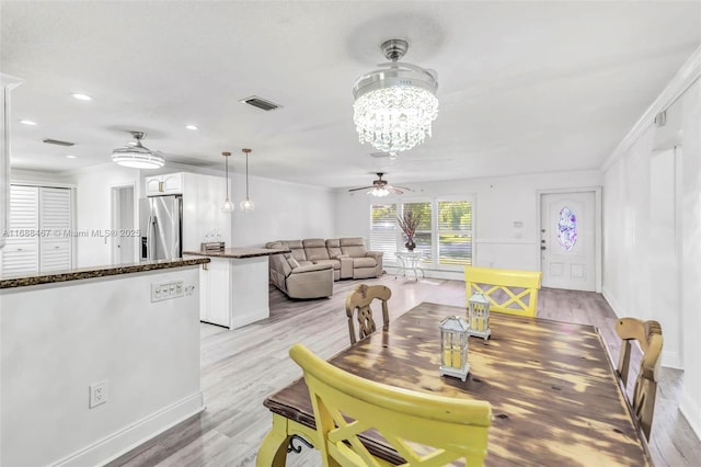 dining space with ceiling fan with notable chandelier, ornamental molding, and light hardwood / wood-style flooring