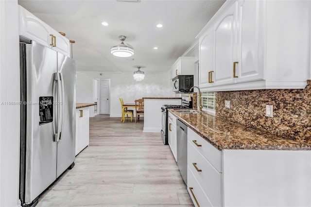 kitchen with decorative backsplash, appliances with stainless steel finishes, dark stone counters, white cabinets, and light hardwood / wood-style floors