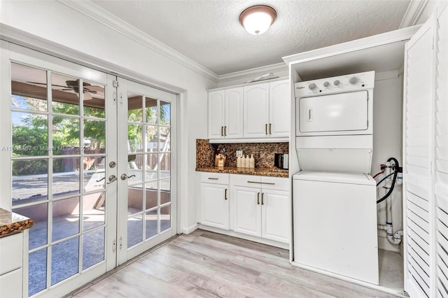 laundry area featuring cabinets, french doors, ornamental molding, a textured ceiling, and stacked washer / drying machine