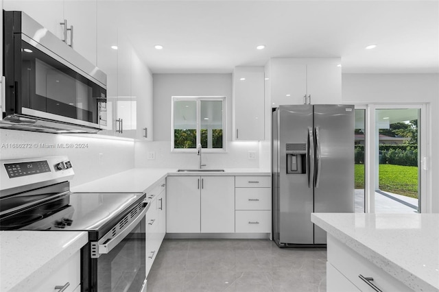 kitchen with white cabinets, sink, decorative backsplash, light stone counters, and stainless steel appliances