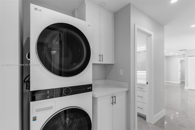 laundry area with stacked washer / dryer, light tile patterned floors, and cabinets