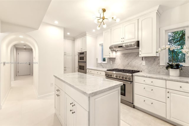 kitchen with light tile patterned floors, appliances with stainless steel finishes, decorative backsplash, a kitchen island, and white cabinets