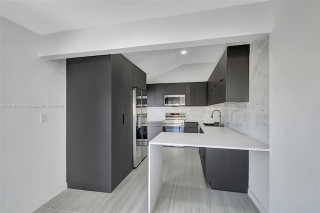 kitchen featuring a kitchen breakfast bar, sink, vaulted ceiling, kitchen peninsula, and stainless steel appliances