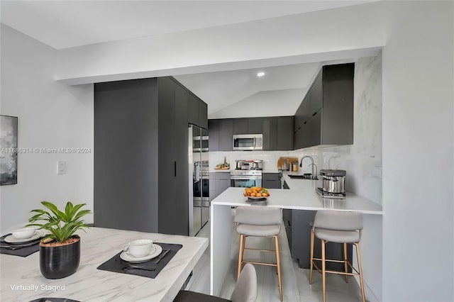 kitchen featuring sink, decorative backsplash, a kitchen bar, kitchen peninsula, and stainless steel appliances