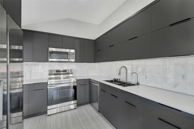 kitchen featuring appliances with stainless steel finishes, tasteful backsplash, vaulted ceiling, sink, and light tile patterned floors