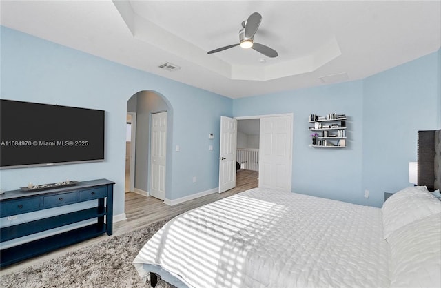 bedroom featuring light wood-type flooring, a tray ceiling, and ceiling fan