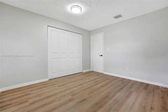 unfurnished bedroom with light hardwood / wood-style flooring, a textured ceiling, and a closet