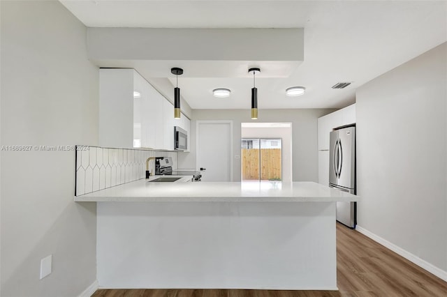 kitchen with kitchen peninsula, white cabinets, pendant lighting, and appliances with stainless steel finishes