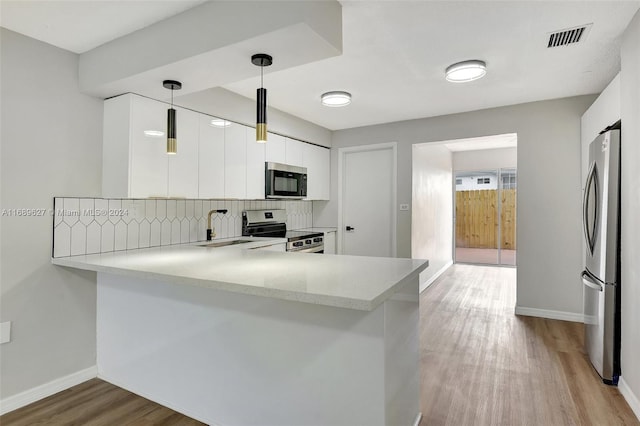 kitchen featuring white cabinetry, kitchen peninsula, appliances with stainless steel finishes, and pendant lighting