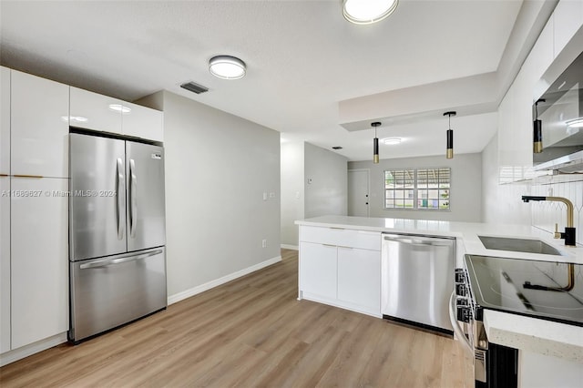 kitchen with hanging light fixtures, white cabinets, light wood-type flooring, and appliances with stainless steel finishes