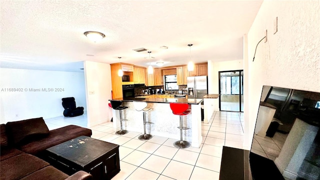 kitchen featuring black appliances, a breakfast bar area, light tile patterned floors, decorative light fixtures, and decorative backsplash