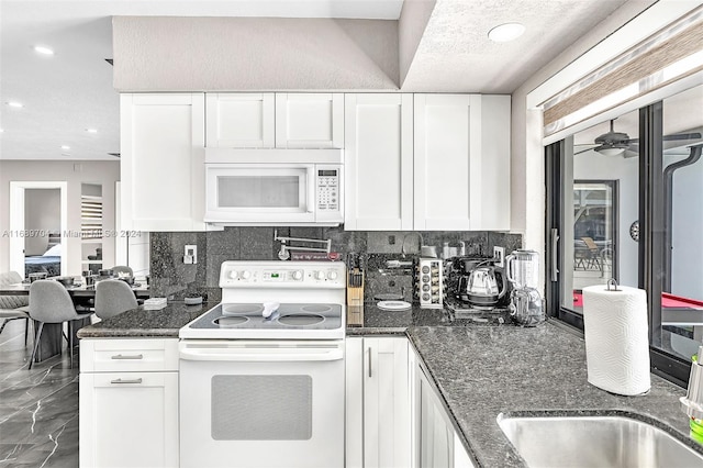 kitchen with backsplash, white cabinets, dark stone countertops, white appliances, and ceiling fan