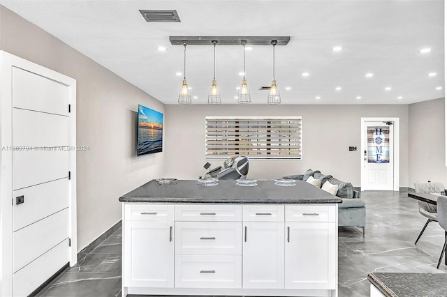 kitchen with pendant lighting, white cabinetry, a center island with sink, and dark stone countertops