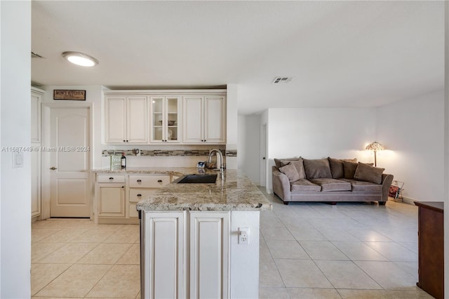 kitchen with light stone countertops, kitchen peninsula, sink, and light tile patterned floors