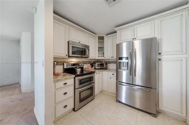 kitchen with light tile patterned flooring, light stone counters, backsplash, and appliances with stainless steel finishes