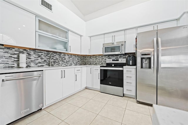 kitchen with tasteful backsplash, light tile patterned flooring, white cabinetry, appliances with stainless steel finishes, and sink