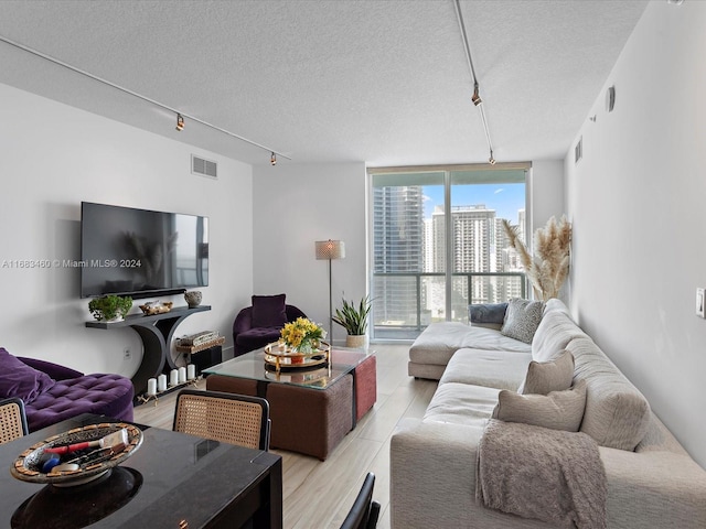 living room featuring light hardwood / wood-style flooring, rail lighting, a textured ceiling, and floor to ceiling windows