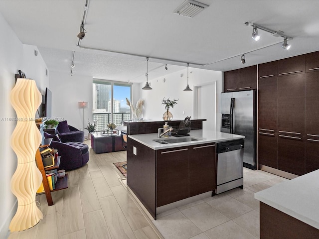 kitchen featuring a center island with sink, appliances with stainless steel finishes, track lighting, hanging light fixtures, and sink