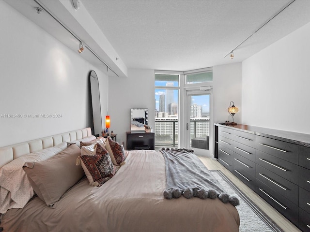 bedroom featuring light hardwood / wood-style floors, track lighting, access to exterior, a textured ceiling, and a wall of windows