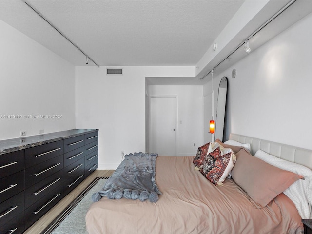 bedroom featuring a textured ceiling, light hardwood / wood-style floors, and rail lighting