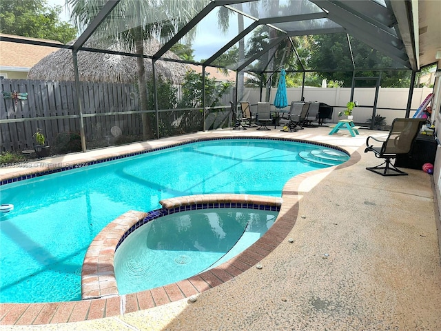 view of pool with glass enclosure, a patio area, and an in ground hot tub