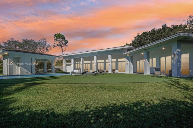 back house at dusk featuring a lawn