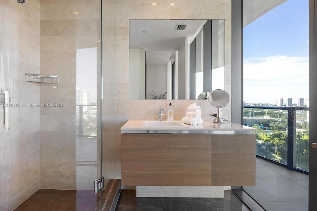 bathroom with vanity, expansive windows, a shower with door, and tile walls