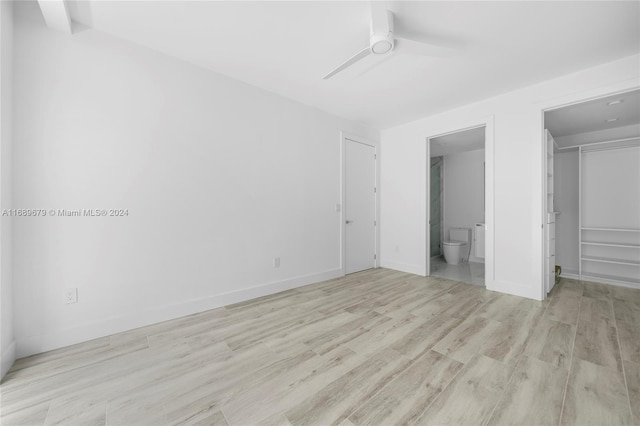 unfurnished bedroom with ensuite bath, light hardwood / wood-style flooring, ceiling fan, a closet, and a spacious closet