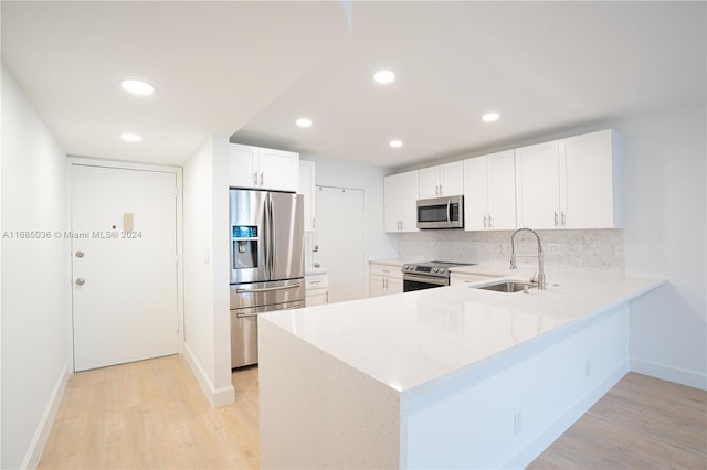 kitchen with stainless steel appliances, white cabinetry, backsplash, sink, and light hardwood / wood-style flooring