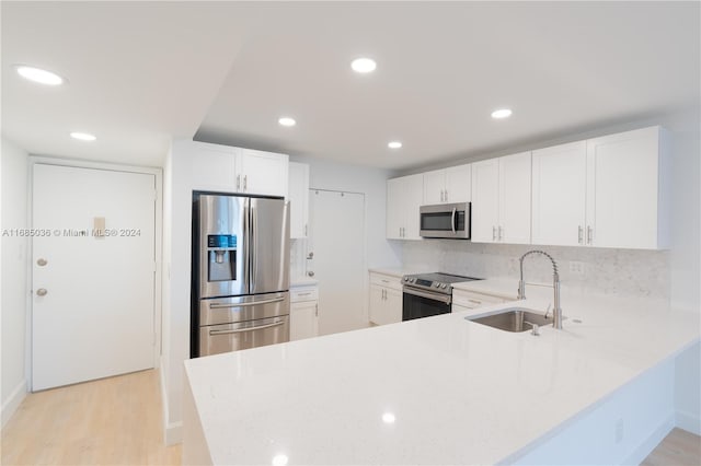 kitchen with stainless steel appliances, white cabinetry, decorative backsplash, sink, and light hardwood / wood-style flooring