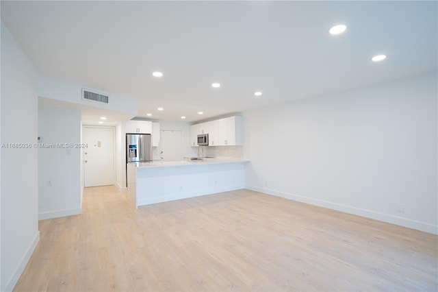 kitchen featuring white cabinetry, appliances with stainless steel finishes, kitchen peninsula, backsplash, and light hardwood / wood-style flooring