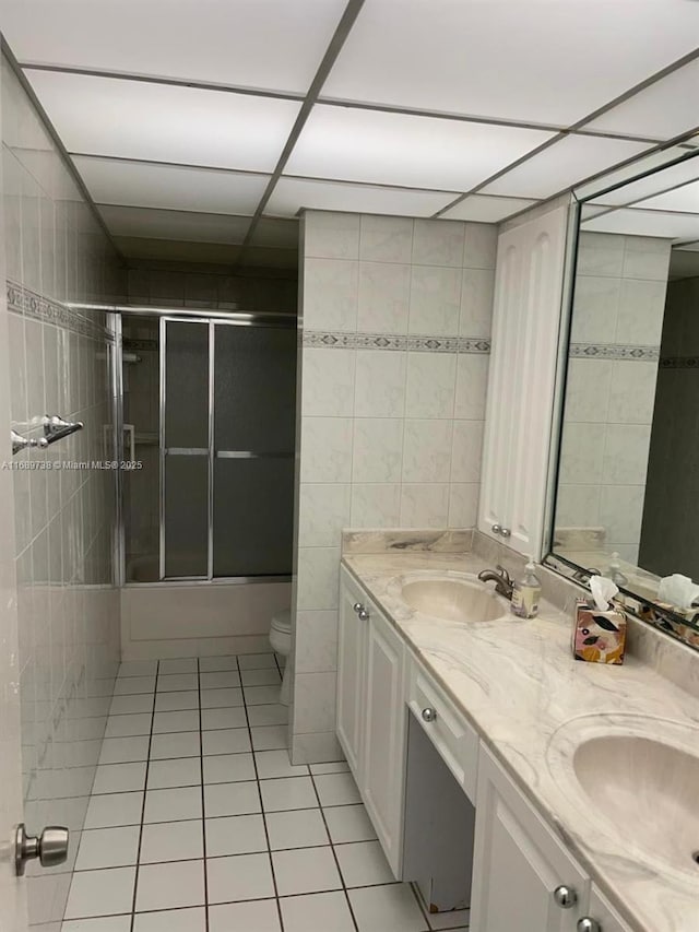 full bathroom featuring tile patterned flooring, combined bath / shower with glass door, toilet, vanity, and tile walls