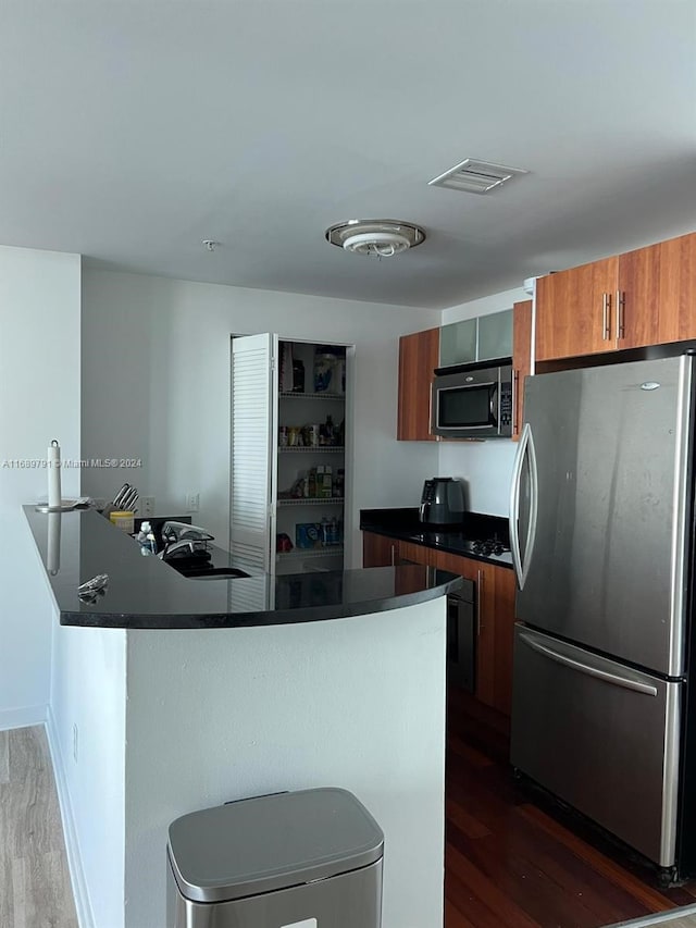 kitchen with kitchen peninsula, appliances with stainless steel finishes, a kitchen breakfast bar, sink, and dark hardwood / wood-style floors