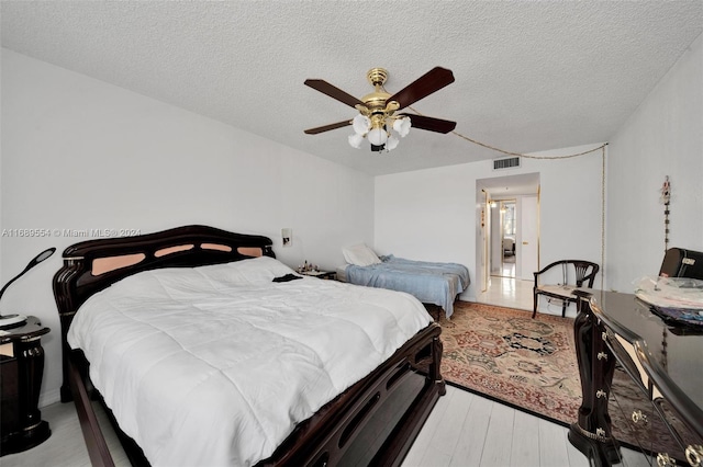 bedroom with ceiling fan, a textured ceiling, and light hardwood / wood-style floors