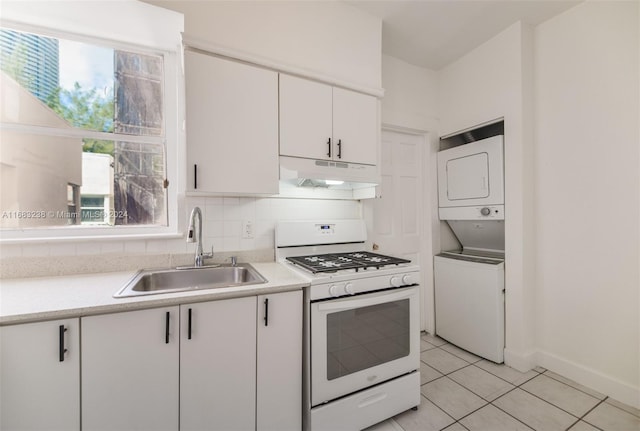 kitchen featuring white gas stove, stacked washer and clothes dryer, sink, white cabinets, and decorative backsplash