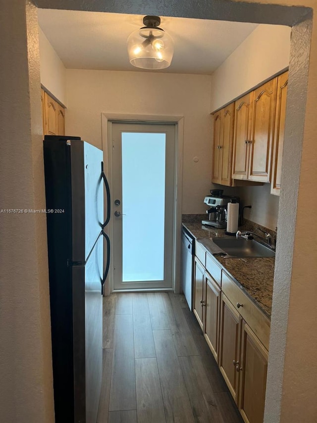 kitchen with dark hardwood / wood-style floors, black refrigerator, sink, dishwasher, and dark stone countertops