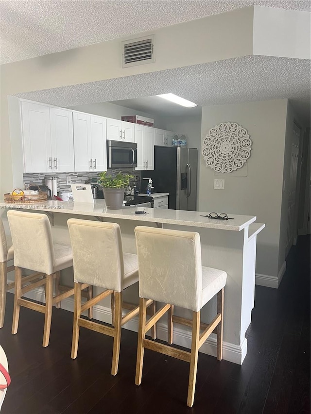 kitchen featuring stainless steel appliances, kitchen peninsula, dark hardwood / wood-style floors, a breakfast bar, and white cabinetry