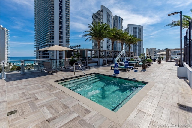 view of swimming pool featuring a patio, a water view, and a hot tub