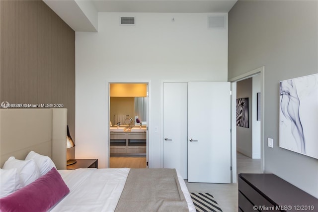 bedroom with light hardwood / wood-style floors, ensuite bath, and a towering ceiling