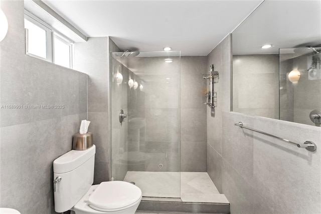 bathroom with toilet, tiled shower, and tile walls