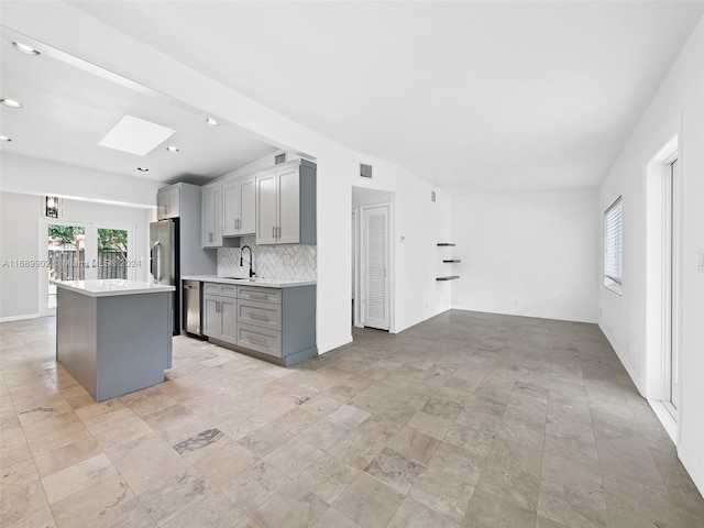 kitchen with stainless steel appliances, a center island, decorative backsplash, gray cabinetry, and lofted ceiling with skylight