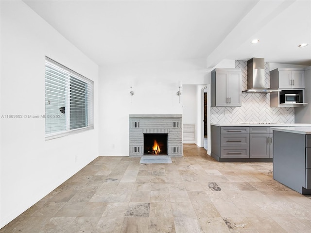 kitchen featuring a fireplace, gray cabinets, wall chimney exhaust hood, and tasteful backsplash