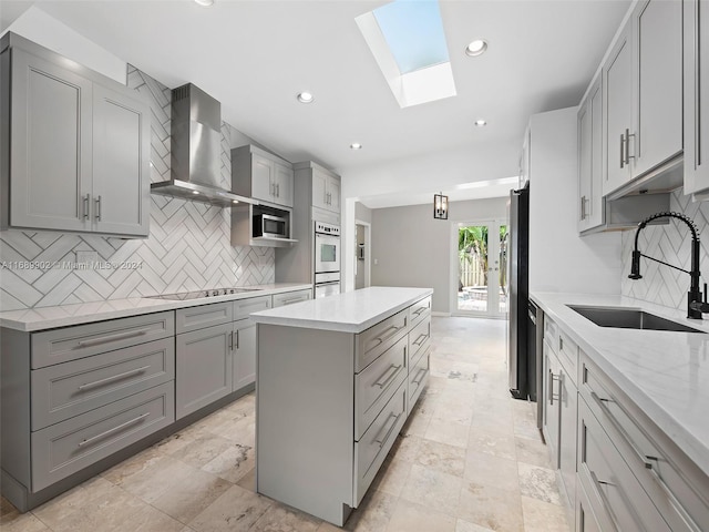 kitchen featuring gray cabinets, a skylight, sink, and wall chimney exhaust hood