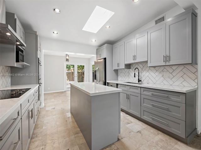 kitchen featuring stainless steel appliances, sink, a skylight, a kitchen island, and gray cabinetry