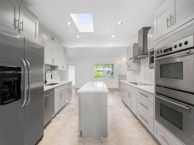 kitchen featuring sink, appliances with stainless steel finishes, wall chimney exhaust hood, backsplash, and a kitchen island