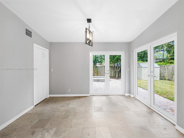 empty room featuring lofted ceiling, a healthy amount of sunlight, an inviting chandelier, and french doors